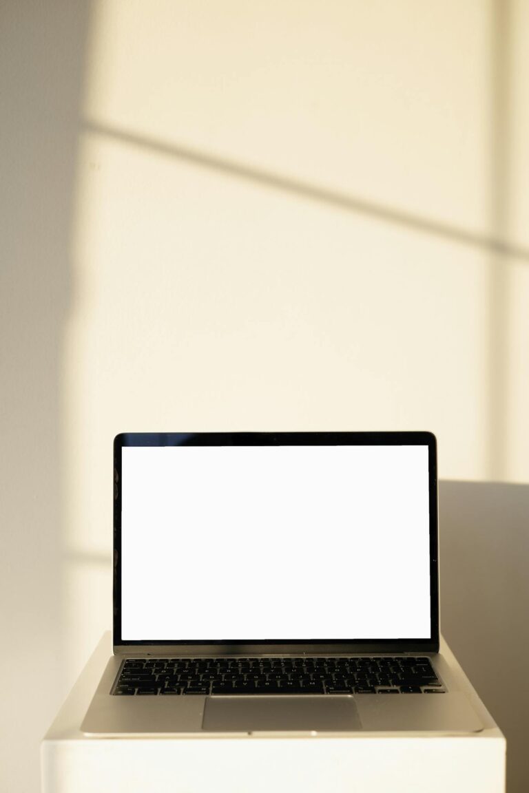 A sleek laptop with a blank screen, perfect for mockups, set against a sunlit wall for a minimalist aesthetic.
